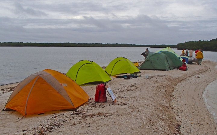 a group of tents rest on a sandy peninsula on an outward bound course 